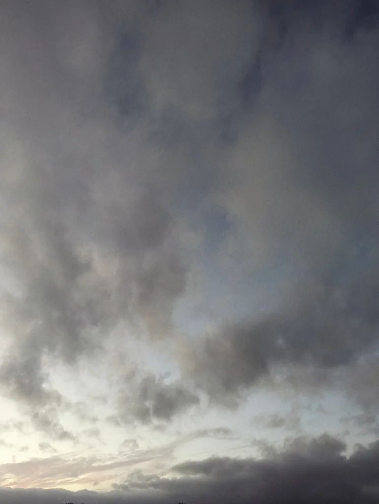 Moody grey and blue clouds filling the sky at twilight with a sliver of sunset light along the bottom horizon.