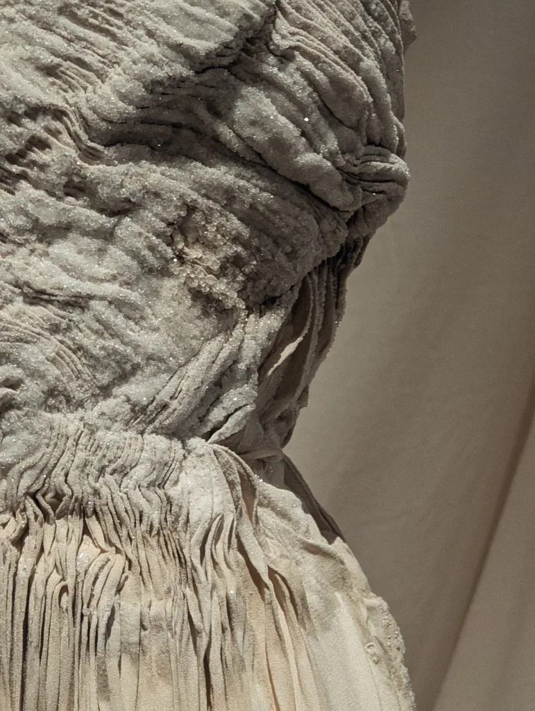 Detailed view of a cream pleated garment encrusted with thick, sparkling white crystalline formations.
