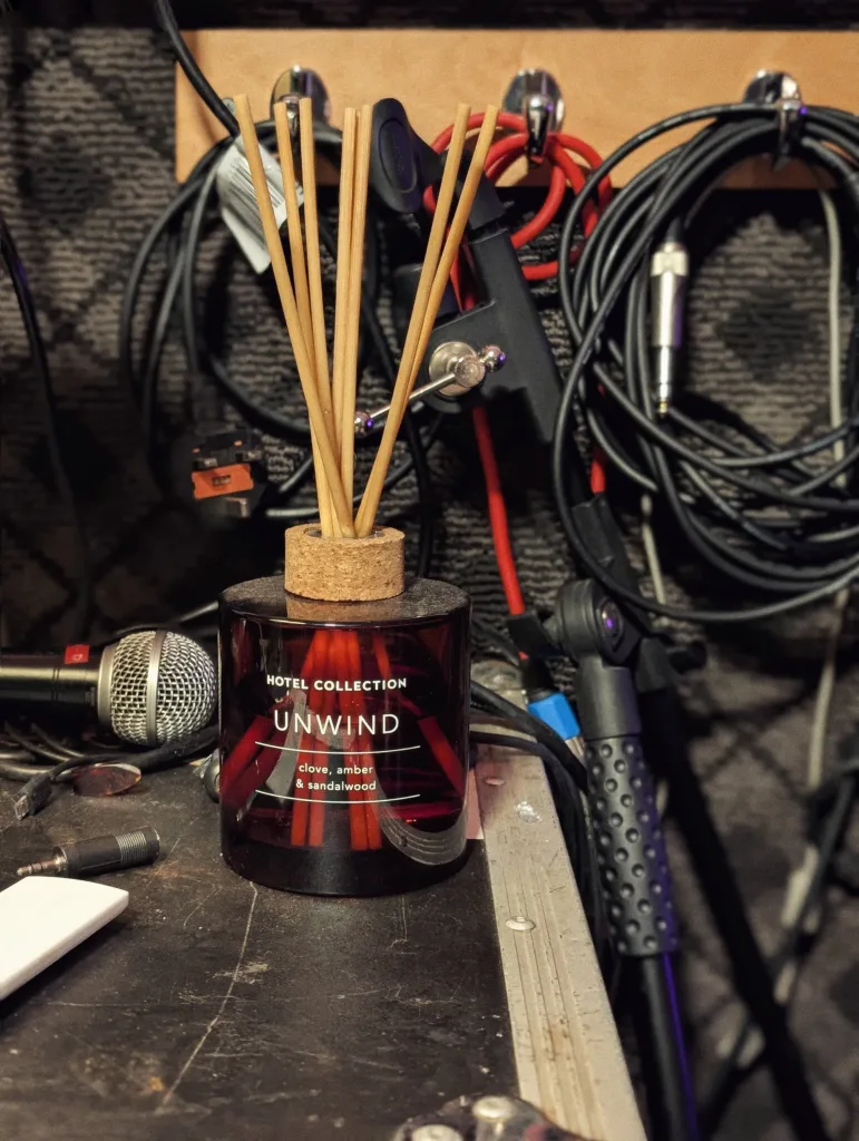 A red glass "Unwind" reed diffuser sits on a road case, surrounded by coiled audio cables and a microphone in a studio.