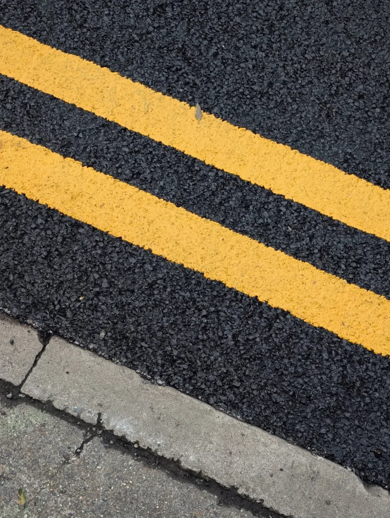 Close-up of double yellow road markings painted diagonally across dark tarmac