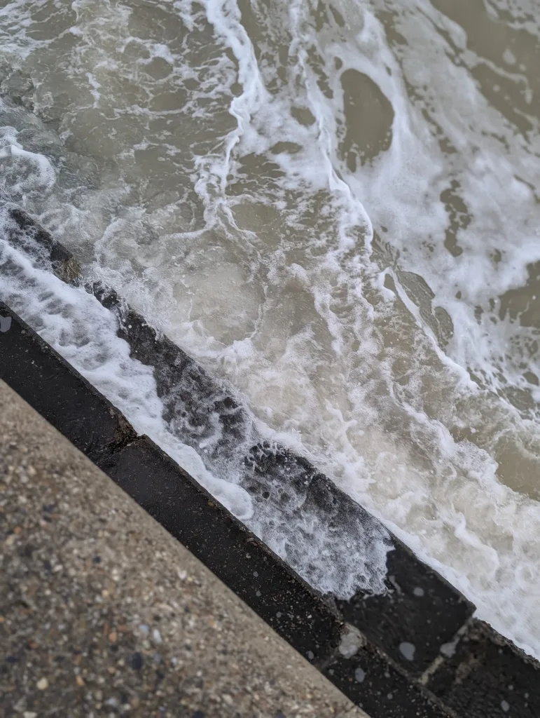 White sea foam and churning grey water crashing against a dark concrete ledge.