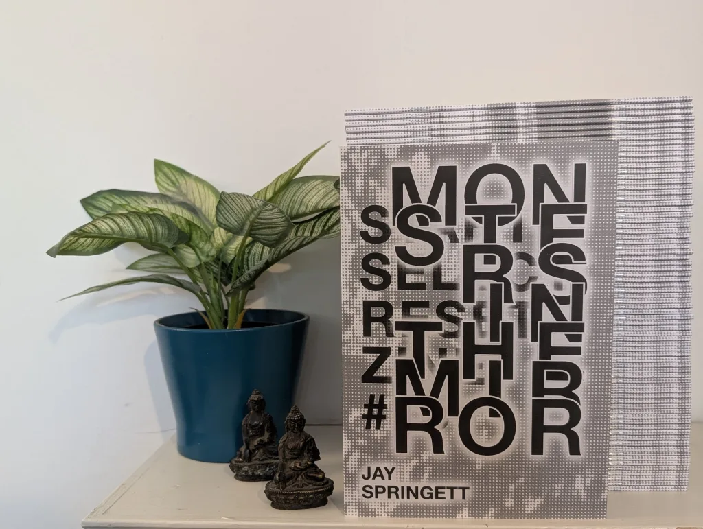 Featured image for Start Select Reset Issue 15: Monsters in the Mirror - the zine by Jay Springett propped up next to a potted plant and two small figurines.