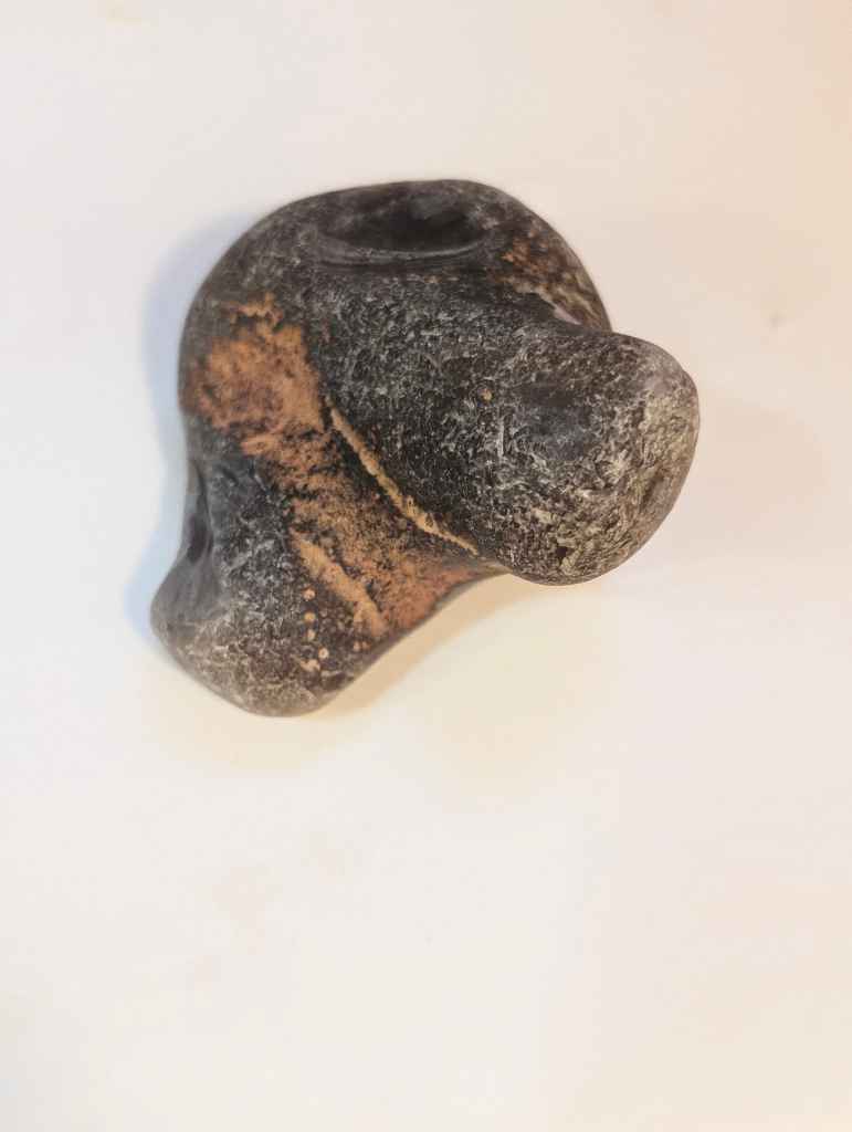 A dark grey and brown stone naturally resembling the head of a dog, set against a plain off-white background