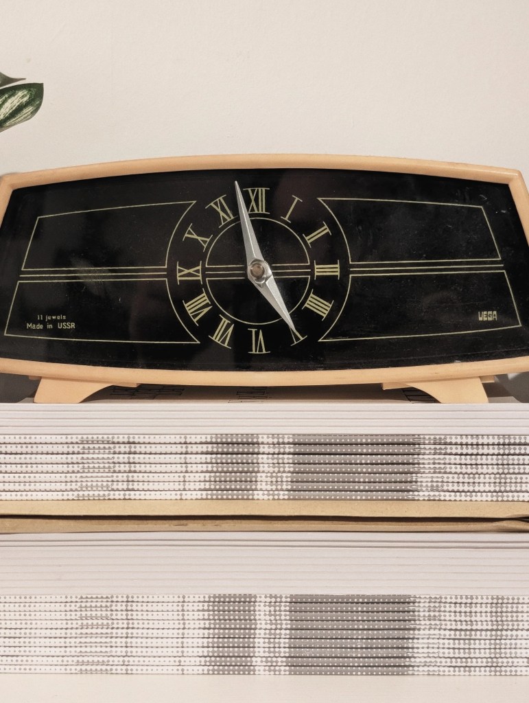 Vintage Vega mantel clock with Roman numerals and "Made in USSR" text, resting on top of two stacked white books.